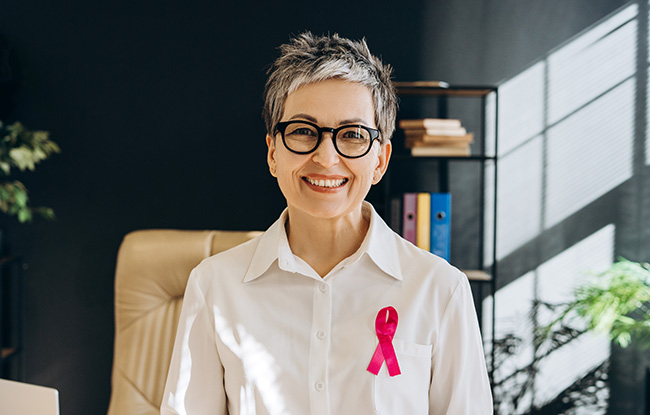 Smiling senior professional woman wearing pink ribbon supporting breast cancer awareness