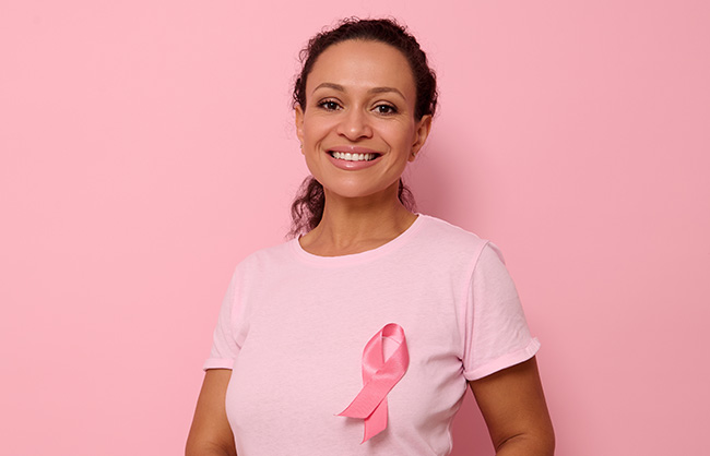 Smiling mixed race woman in pink T-shirt with pink satin ribbon symbolizing International Breast Cancer Day, expressing solidarity and support for breast cancer patients and survivors. 1 st october