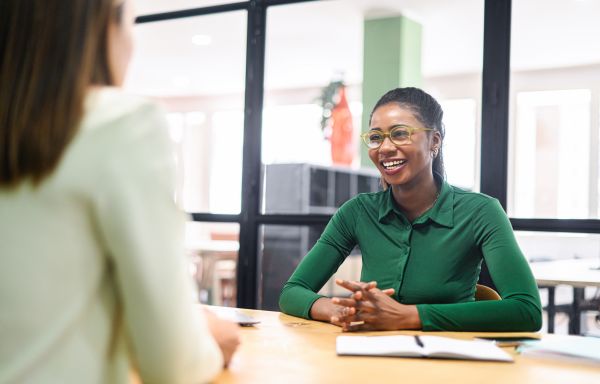 Female manager praises young ambitious african-american female employee sitting in contemporary office space