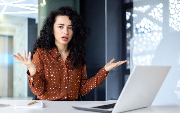 Frustrated and sad woman inside office looking at camera, businesswoman unhappy with achievement results working at desk using laptop at work