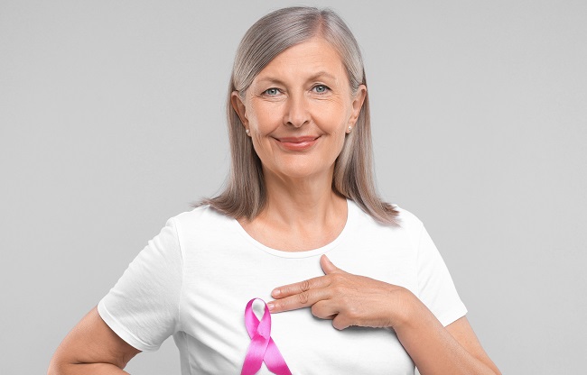 Beautiful senior woman with pink ribbon on light grey background. Breast cancer awareness